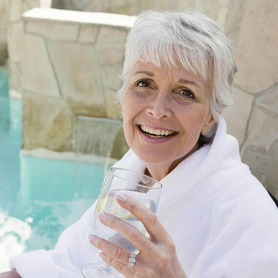 About Us Senior woman enjoying a glass of water with lemon slice by the pool