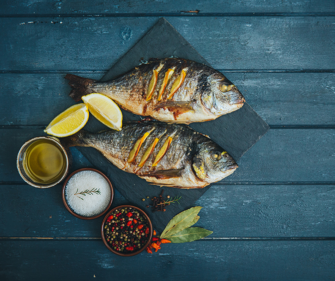 Chef prepared grilled whole fish with lemon wedges and coarse salt and pepercorns