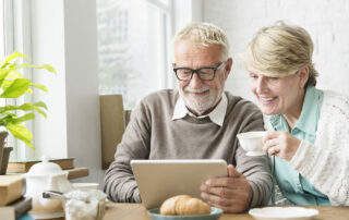 Senior couple smiling and looking at tablet while sitting at a table