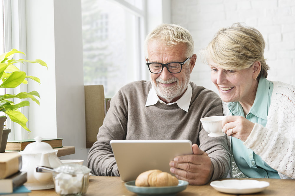 Senior couple smiling and looking at tablet while sitting at a table