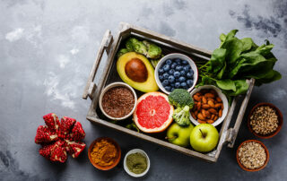 Wooden tray with a variety of fruits and vegetables arranged on it and beside it on a grey marble countertop
