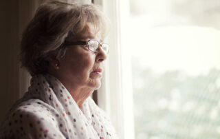 Senior woman with glasses looking worried out the window