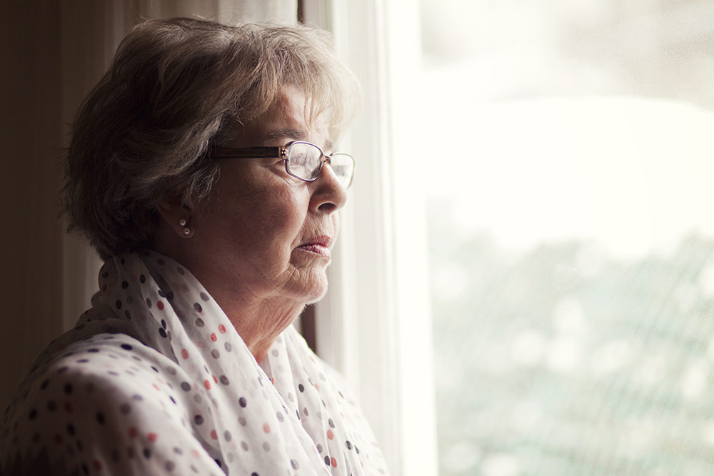 Senior woman with glasses looking worried out the window