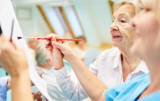 Senior woman painting with instructors help in art therapy class